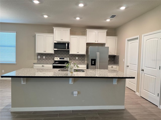 kitchen with a kitchen bar, an island with sink, appliances with stainless steel finishes, light stone counters, and wood-type flooring