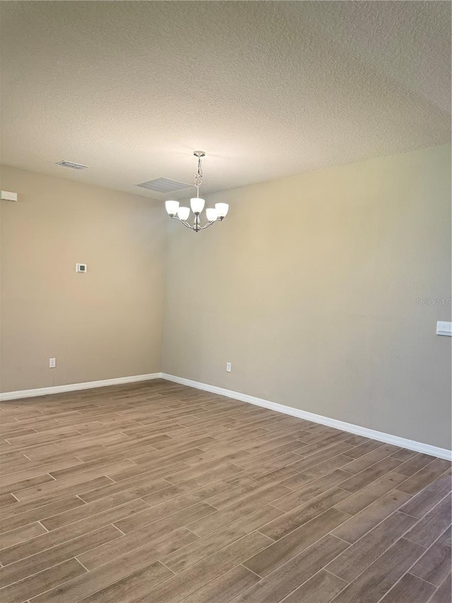 empty room featuring a notable chandelier, wood-type flooring, and a textured ceiling