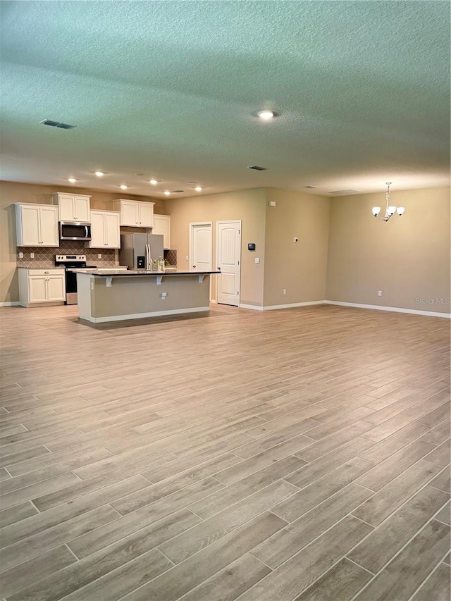 unfurnished living room featuring a chandelier, light hardwood / wood-style floors, and a textured ceiling