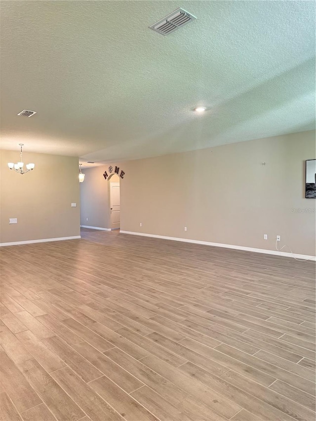 empty room featuring light wood-type flooring, a textured ceiling, and a chandelier