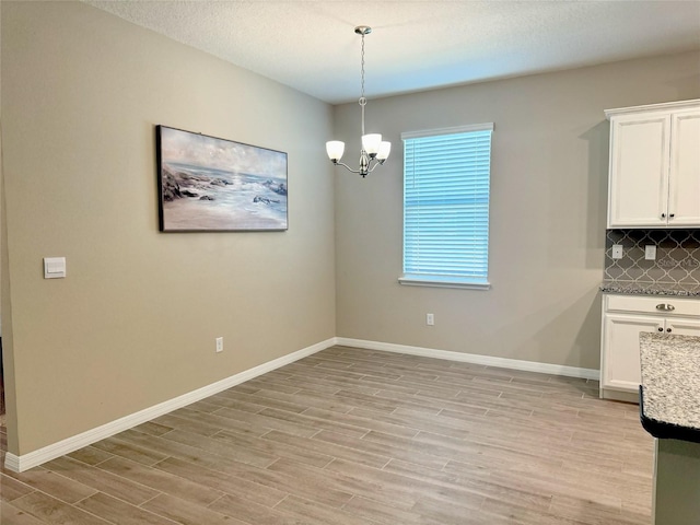 unfurnished dining area with a chandelier, light hardwood / wood-style floors, and a textured ceiling