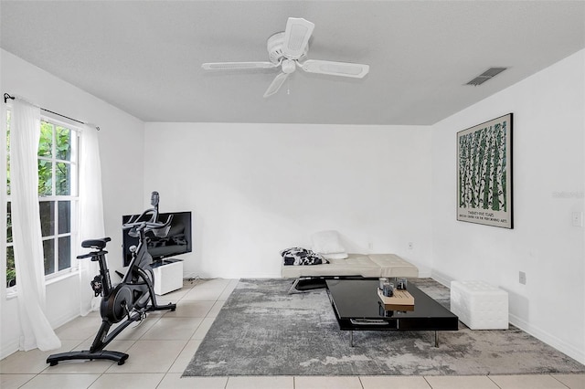 exercise area featuring ceiling fan, light tile patterned flooring, and a textured ceiling