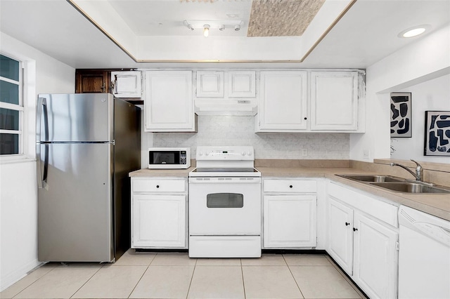 kitchen with a raised ceiling, sink, white cabinets, and white appliances