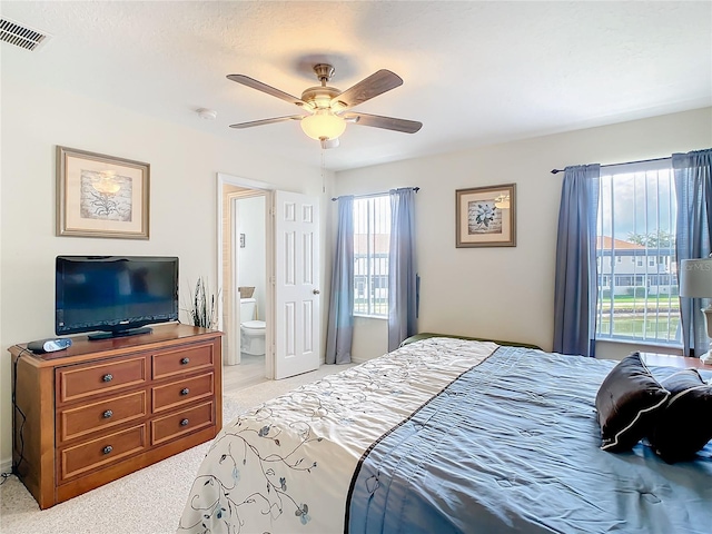 bedroom with ceiling fan, light colored carpet, and ensuite bathroom