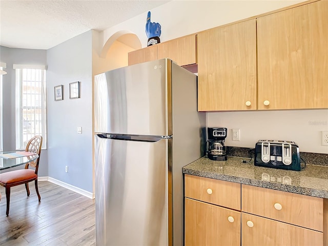 kitchen featuring stainless steel fridge, a textured ceiling, light hardwood / wood-style floors, and dark stone countertops