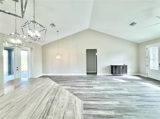 unfurnished living room with an inviting chandelier, hardwood / wood-style floors, french doors, and lofted ceiling