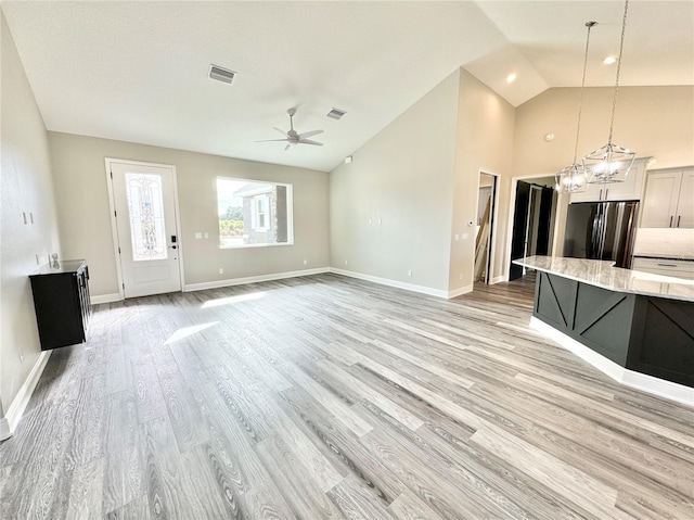 unfurnished living room featuring high vaulted ceiling, light hardwood / wood-style floors, and ceiling fan with notable chandelier