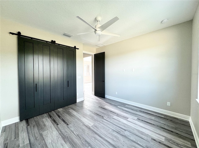 unfurnished bedroom featuring ceiling fan, a barn door, light hardwood / wood-style floors, and a textured ceiling