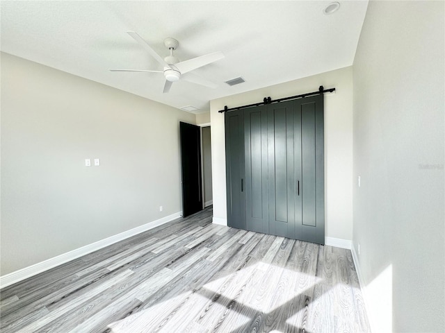 unfurnished bedroom featuring a barn door, ceiling fan, light hardwood / wood-style flooring, and a closet