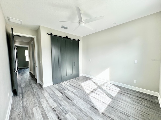 unfurnished bedroom with a barn door, a closet, ceiling fan, and hardwood / wood-style floors