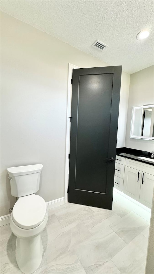 bathroom with tile flooring, vanity, toilet, and a textured ceiling