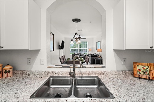 kitchen with hanging light fixtures, light stone countertops, sink, and white cabinetry