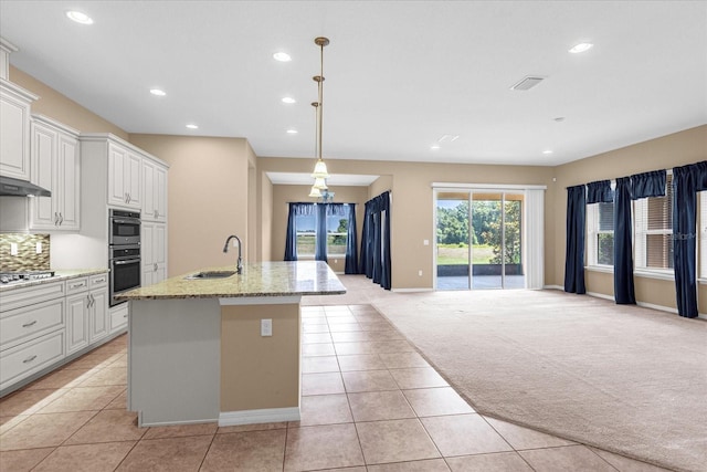 kitchen with sink, white cabinetry, stainless steel appliances, an island with sink, and light carpet