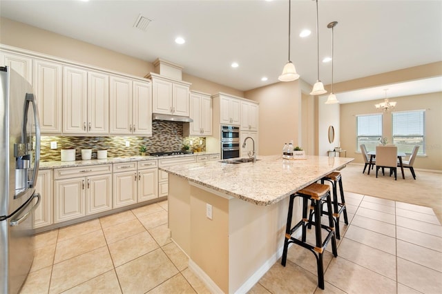 kitchen featuring sink, light stone counters, decorative light fixtures, a center island with sink, and stainless steel appliances