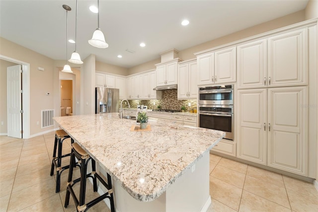 kitchen with pendant lighting, sink, light tile patterned floors, appliances with stainless steel finishes, and a center island with sink