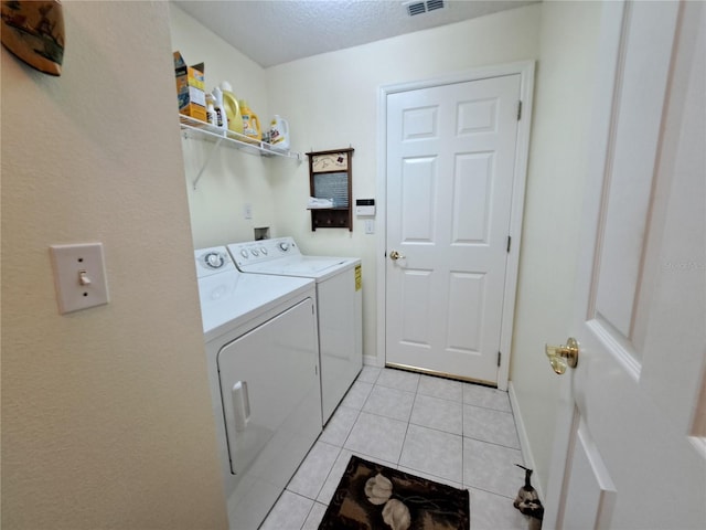 clothes washing area with light tile patterned flooring, washer and dryer, and a textured ceiling