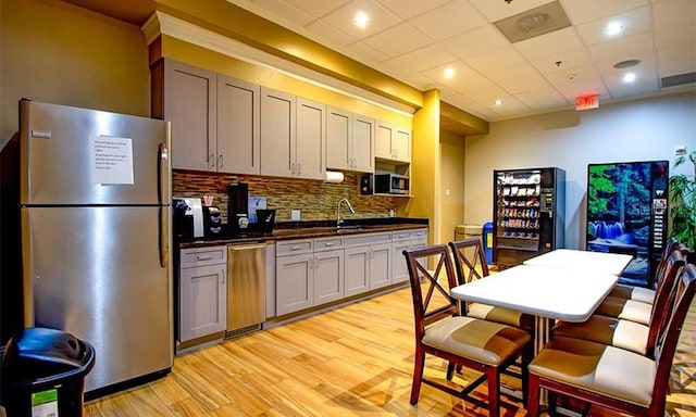 kitchen with gray cabinetry, a paneled ceiling, decorative backsplash, light hardwood / wood-style floors, and stainless steel appliances