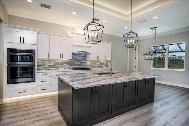 kitchen featuring hanging light fixtures, light hardwood / wood-style flooring, white cabinets, a large island, and sink