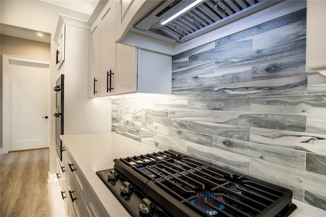 kitchen with white cabinetry, light hardwood / wood-style flooring, premium range hood, stovetop, and tasteful backsplash