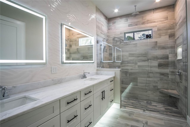 bathroom featuring tile walls, a tile shower, oversized vanity, and dual sinks