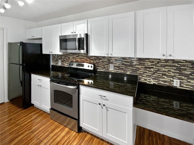 kitchen featuring appliances with stainless steel finishes, tasteful backsplash, dark stone counters, light hardwood / wood-style flooring, and white cabinets