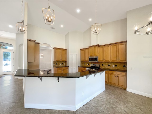 kitchen featuring a kitchen bar, high vaulted ceiling, stainless steel appliances, and decorative light fixtures