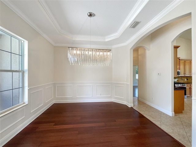 empty room with a chandelier, dark hardwood / wood-style floors, a raised ceiling, and ornamental molding