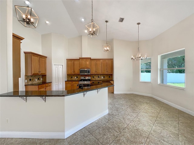 kitchen with a kitchen breakfast bar, backsplash, stainless steel appliances, high vaulted ceiling, and hanging light fixtures