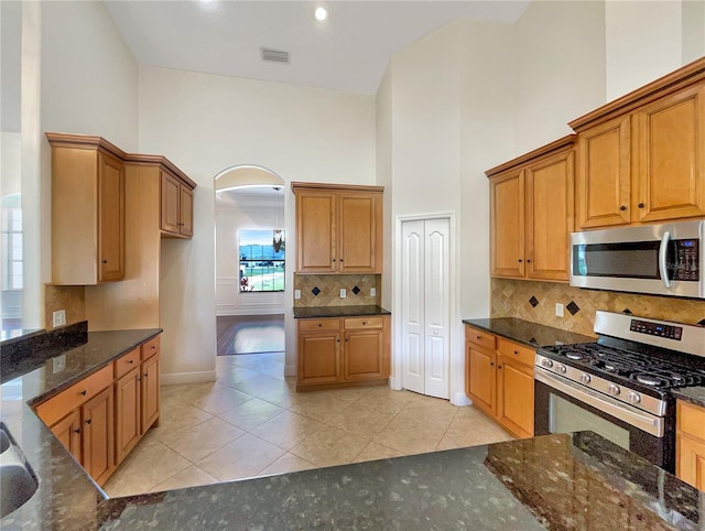 kitchen featuring a wealth of natural light, high vaulted ceiling, dark stone counters, and appliances with stainless steel finishes