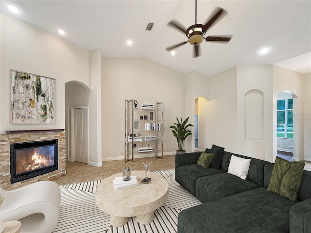 tiled living room featuring ceiling fan, a stone fireplace, and high vaulted ceiling