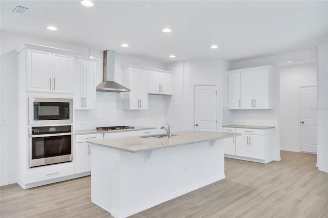 kitchen with a center island with sink, white cabinets, wall chimney range hood, sink, and stainless steel appliances