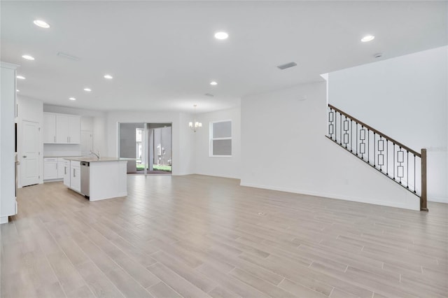 unfurnished living room featuring an inviting chandelier, sink, and light hardwood / wood-style flooring