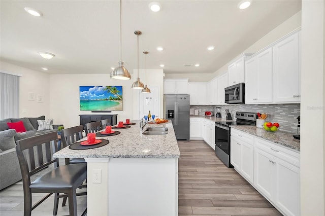 kitchen featuring decorative light fixtures, a kitchen bar, a kitchen island with sink, white cabinets, and appliances with stainless steel finishes