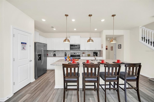 kitchen with decorative backsplash, appliances with stainless steel finishes, a kitchen island with sink, white cabinetry, and hanging light fixtures