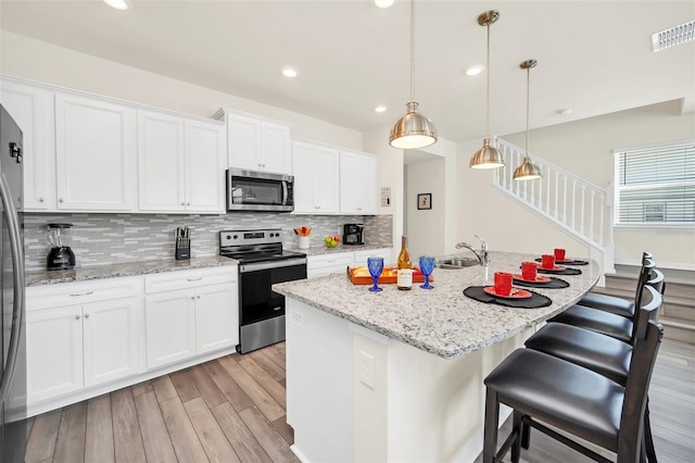 kitchen with a kitchen island with sink, white cabinets, sink, appliances with stainless steel finishes, and decorative light fixtures