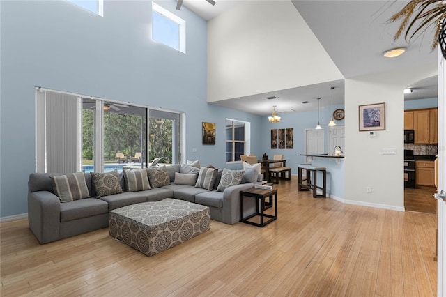 living room with a towering ceiling, ceiling fan with notable chandelier, and light hardwood / wood-style flooring