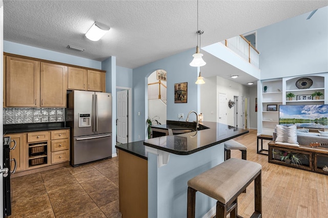 kitchen featuring a kitchen breakfast bar, sink, stainless steel refrigerator with ice dispenser, decorative light fixtures, and dark hardwood / wood-style flooring