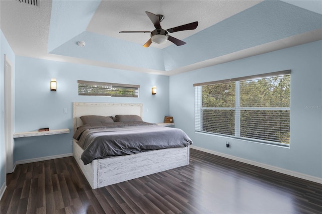 bedroom featuring a raised ceiling, ceiling fan, dark hardwood / wood-style flooring, and a textured ceiling