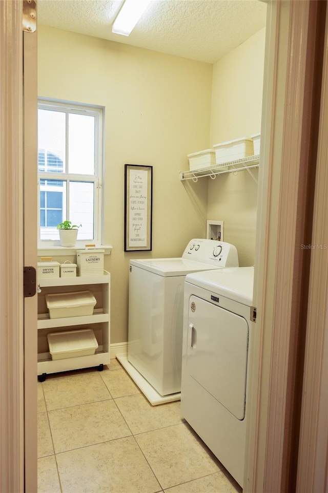 laundry area featuring washing machine and dryer, light tile patterned floors, and a textured ceiling