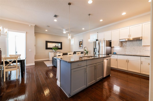 kitchen with dark stone countertops, dark hardwood / wood-style flooring, an island with sink, and appliances with stainless steel finishes