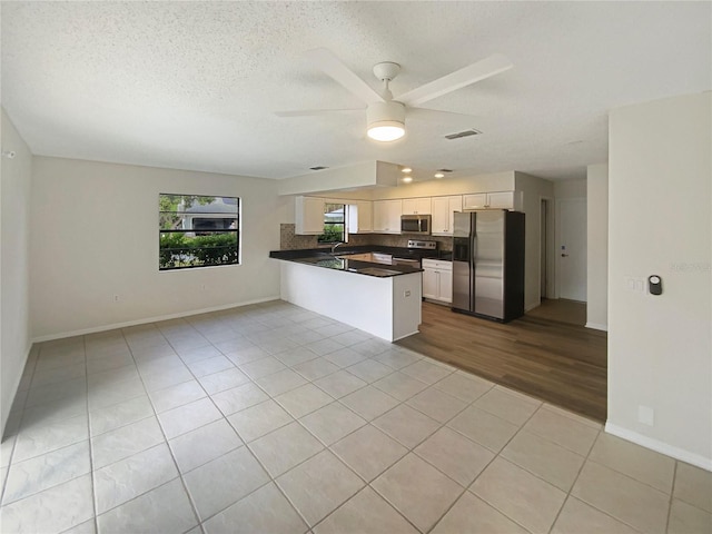 kitchen with white cabinets, ceiling fan, appliances with stainless steel finishes, light tile patterned flooring, and kitchen peninsula