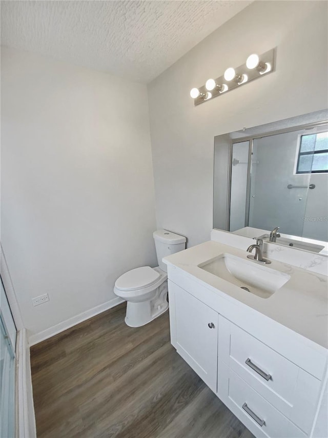 bathroom featuring walk in shower, vanity, a textured ceiling, hardwood / wood-style floors, and toilet