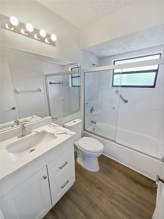 full bathroom with bath / shower combo with glass door, a textured ceiling, toilet, vanity, and hardwood / wood-style flooring