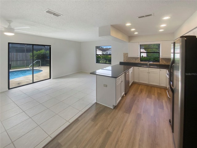 kitchen featuring refrigerator, kitchen peninsula, decorative backsplash, ceiling fan, and white cabinetry