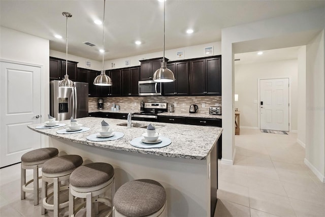 kitchen featuring light tile flooring, stainless steel appliances, backsplash, a center island with sink, and pendant lighting