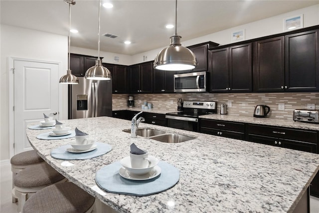 kitchen with decorative light fixtures, light stone counters, backsplash, appliances with stainless steel finishes, and sink