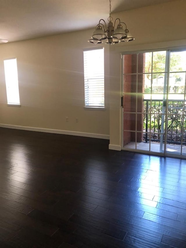 empty room featuring a notable chandelier, a healthy amount of sunlight, and dark wood-type flooring