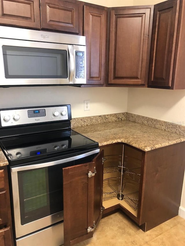 kitchen featuring dark brown cabinetry, light stone countertops, and stainless steel appliances