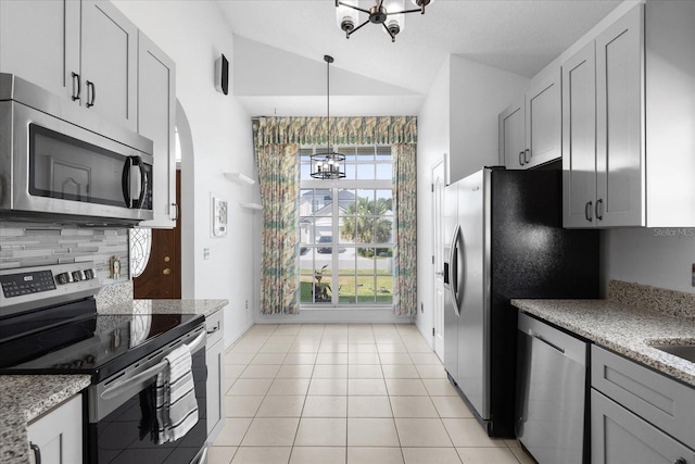 kitchen featuring vaulted ceiling, light tile patterned floors, light stone counters, stainless steel appliances, and a chandelier