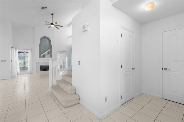 staircase featuring a ceiling fan, tile patterned flooring, visible vents, and a high end fireplace